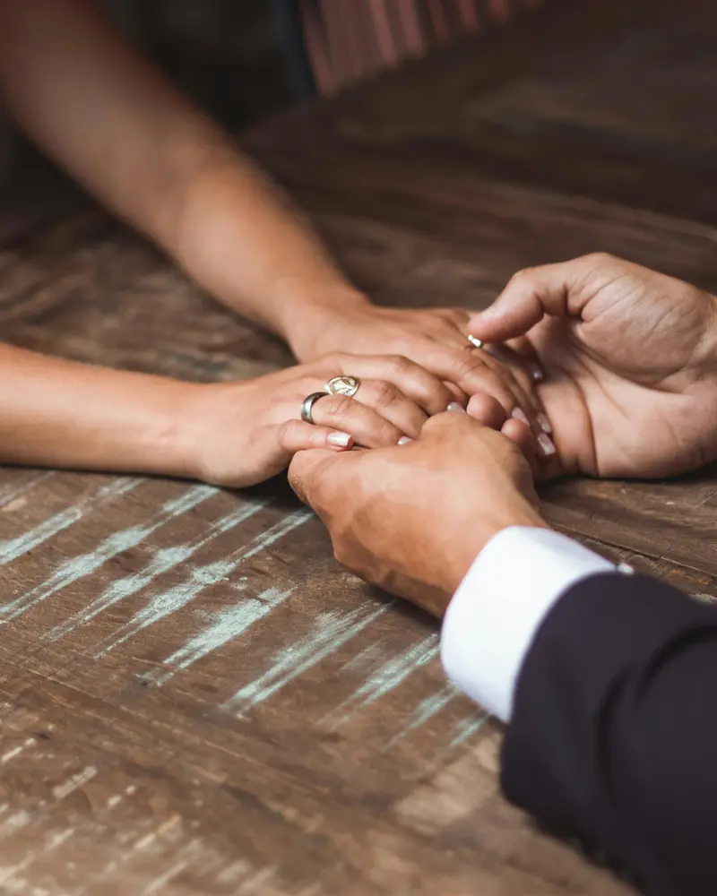 Paar haelt Haende mit Eheringen am Tisch